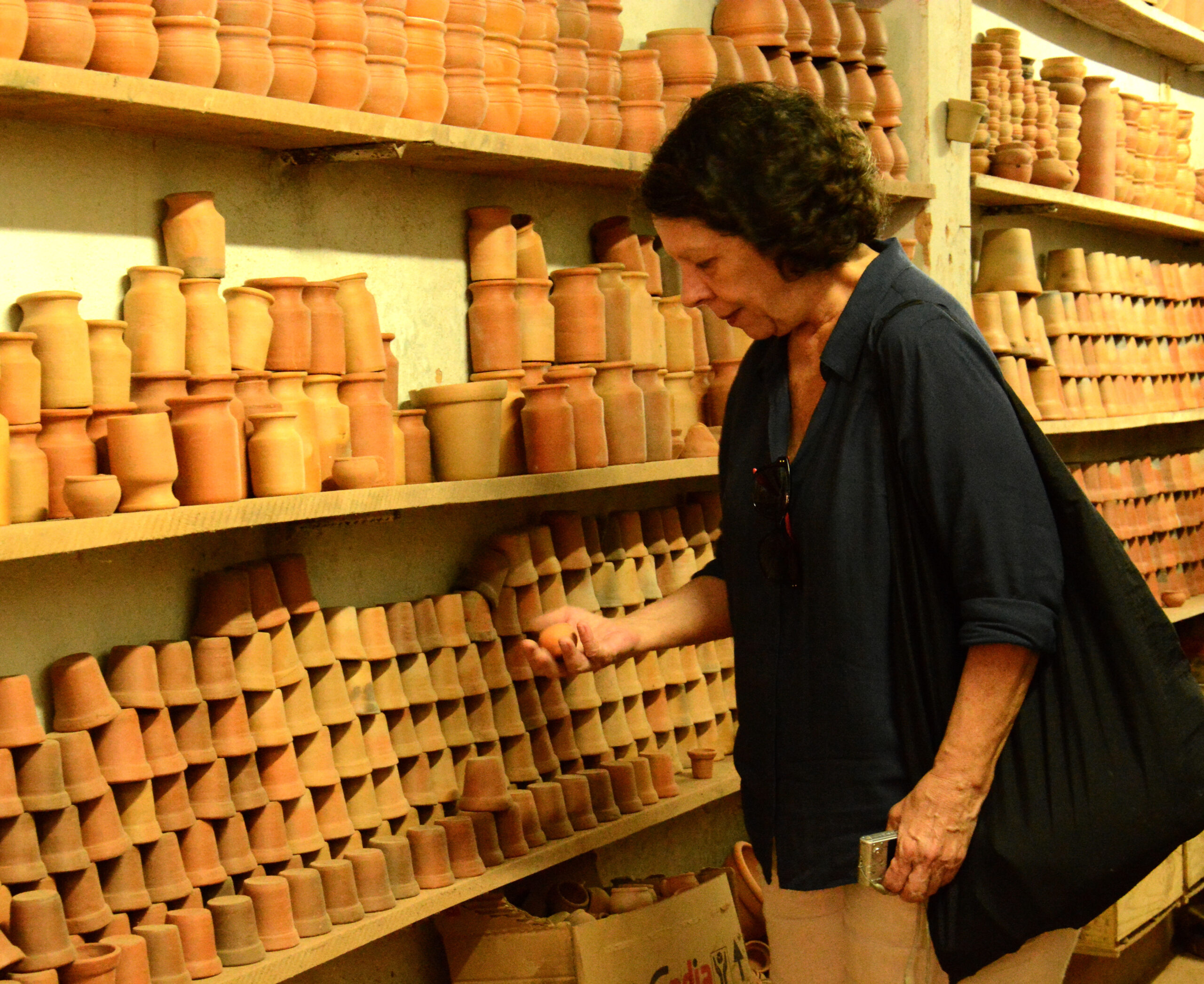 Lorane em uma loja de utensílios de barro. Ela olha para um que segura na mão direita.